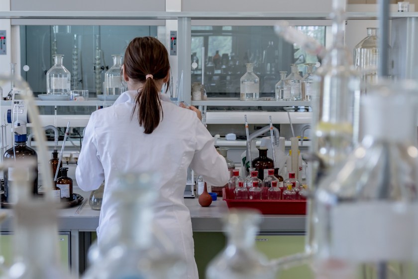 A woman standing at a laboratory bench facing away from the camera and wearing a lab coat